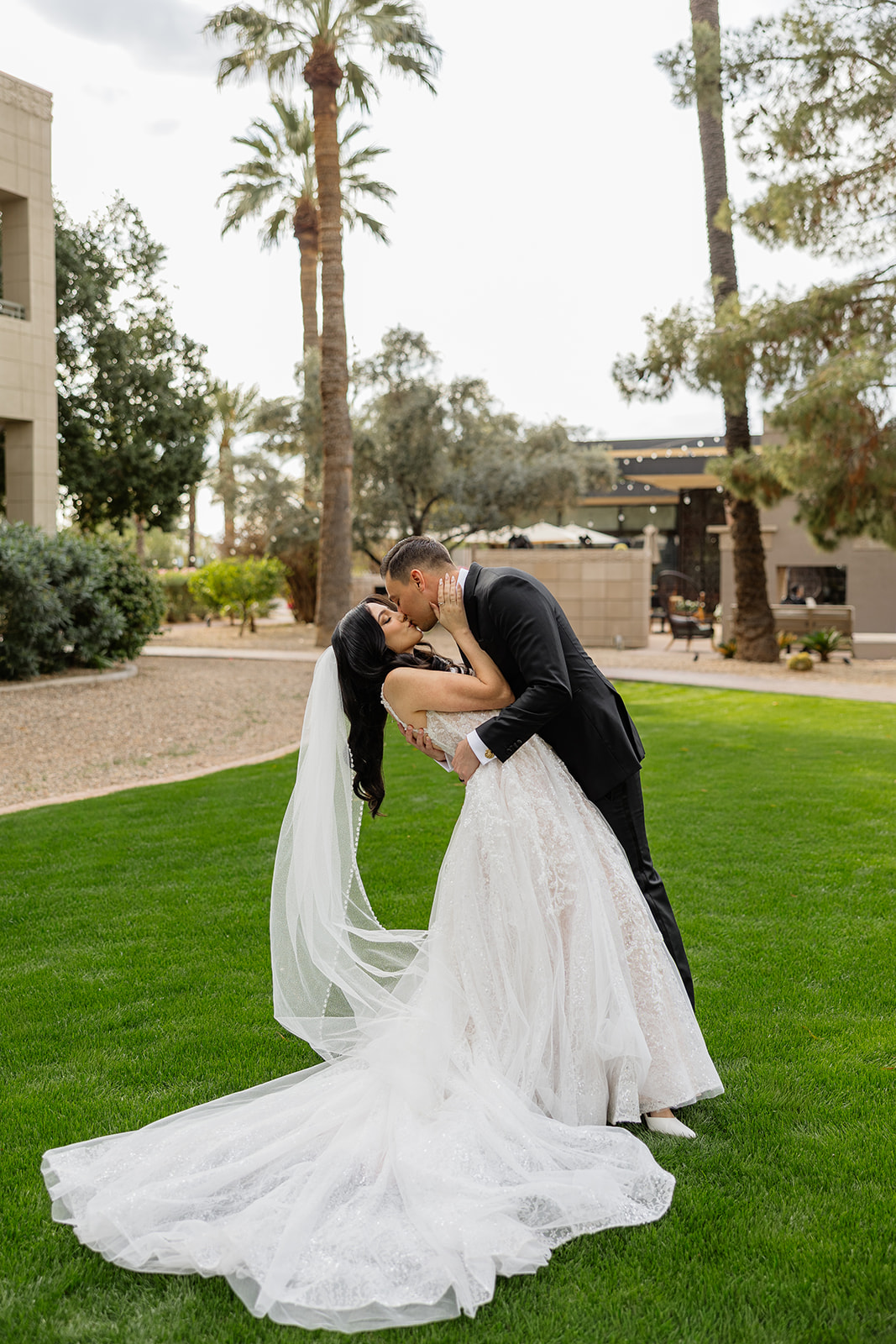 Bride and groom sharing a kiss on the lawn with the bride’s veil trailing behind her
