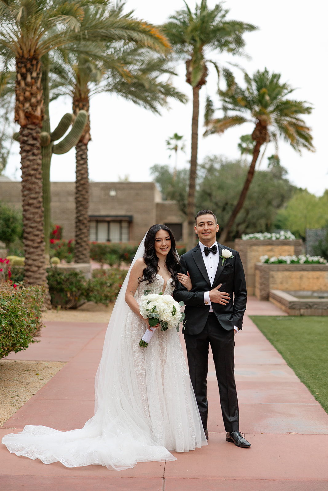 Bride and groom standing arm in arm on a garden path surrounded by palm trees at a Biltmore wedding
