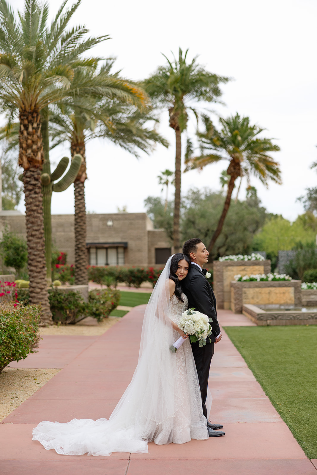 Bride and groom standing back to back on a palm-lined walkway during their Biltmore wedding portraits
