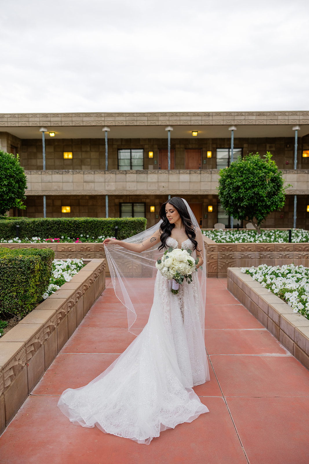 Bride holding her veil and bouquet while standing along a garden walkway at the Biltmore wedding
