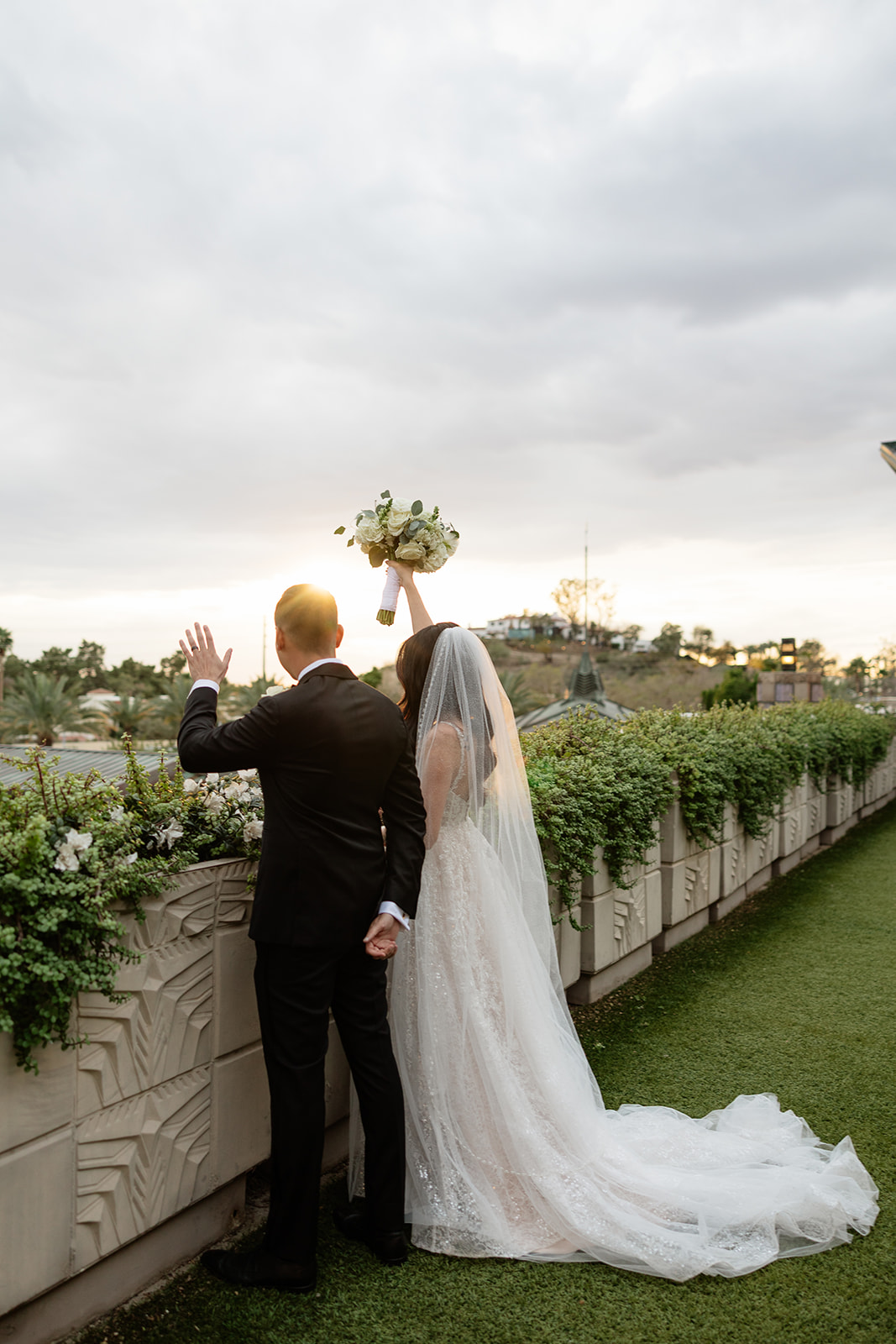 Bride and groom looking out over the view at sunset, bouquet raised, during their Biltmore wedding

