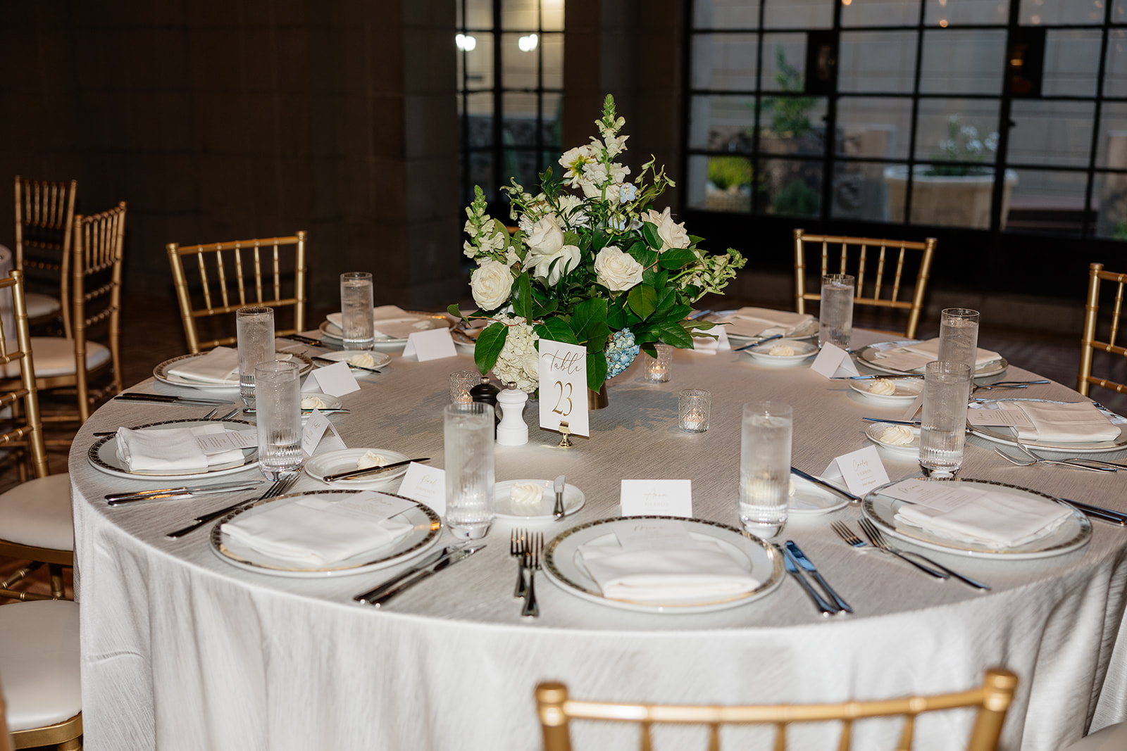 Close-up of a reception table with white place settings and a floral centerpiece
