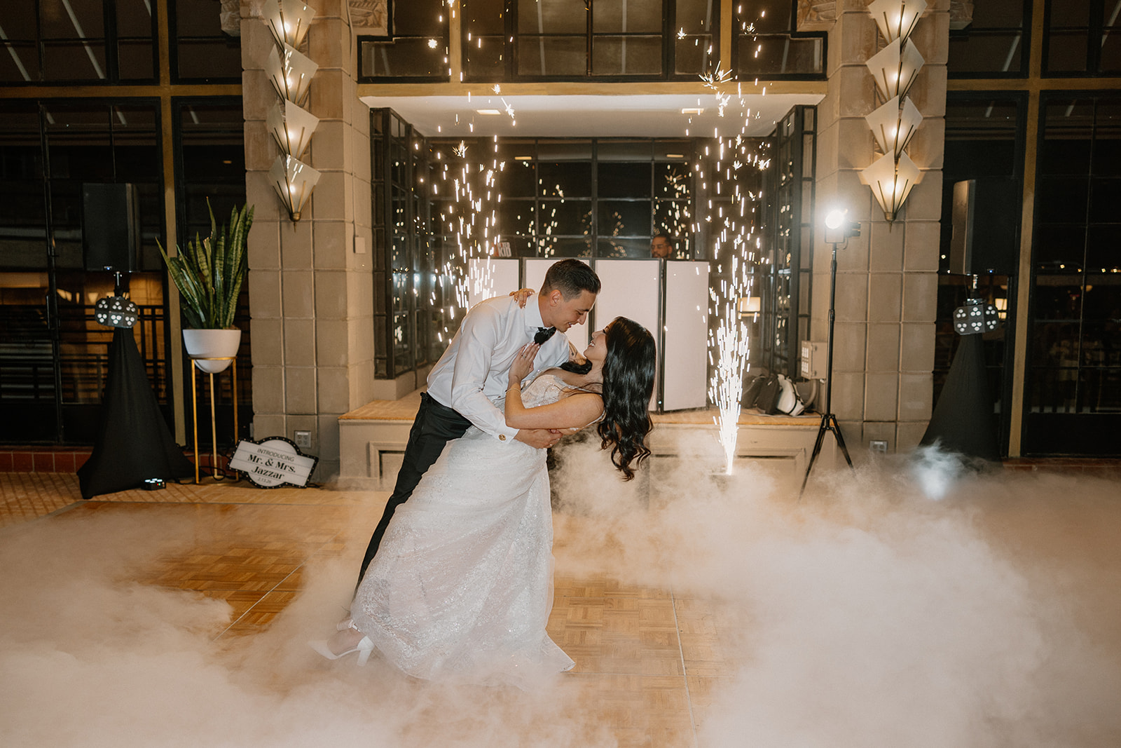 Bride and groom dipping into a kiss surrounded by fog and indoor sparklers during their first dance
