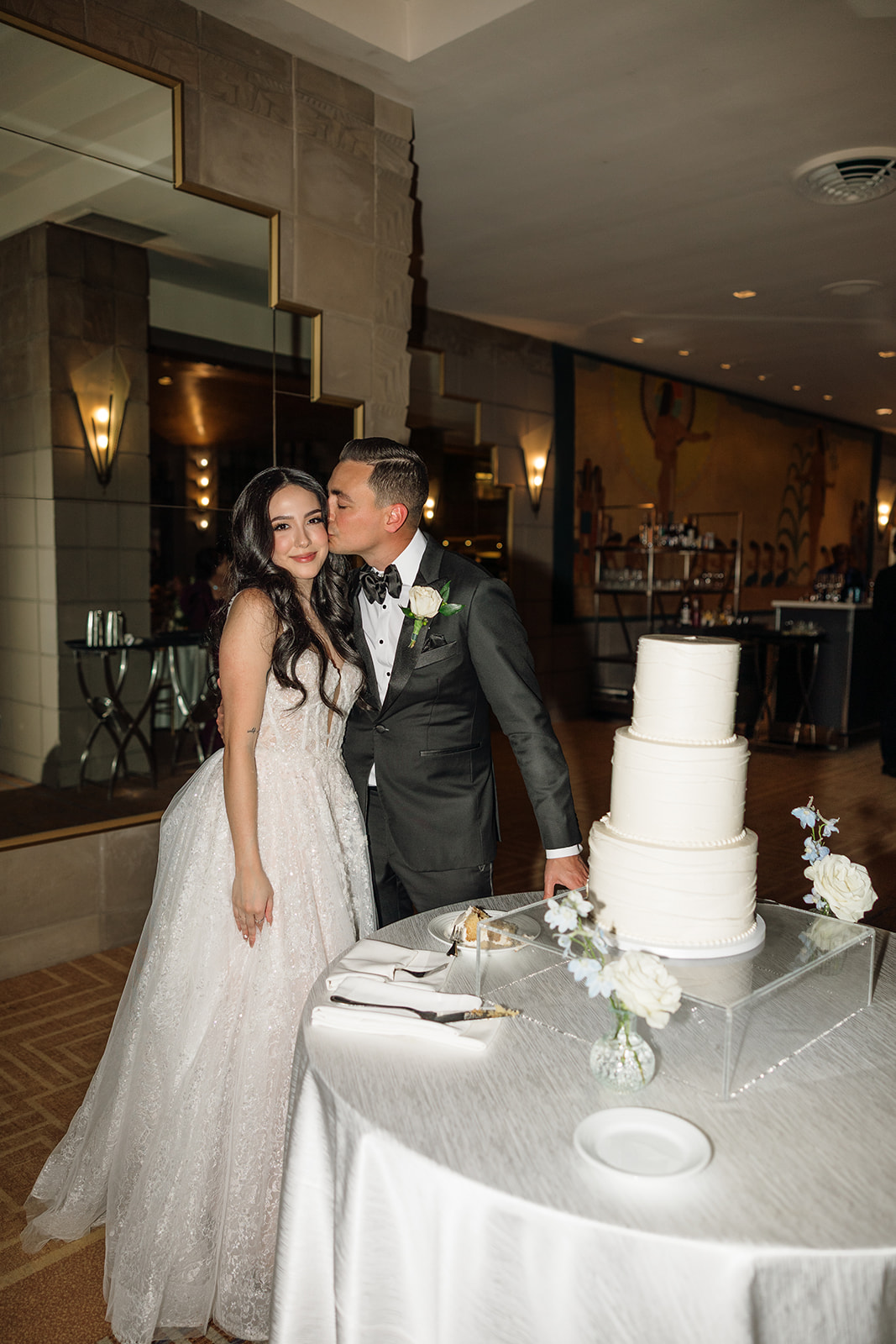Groom kissing the bride’s cheek beside their wedding cake during the Biltmore wedding reception

