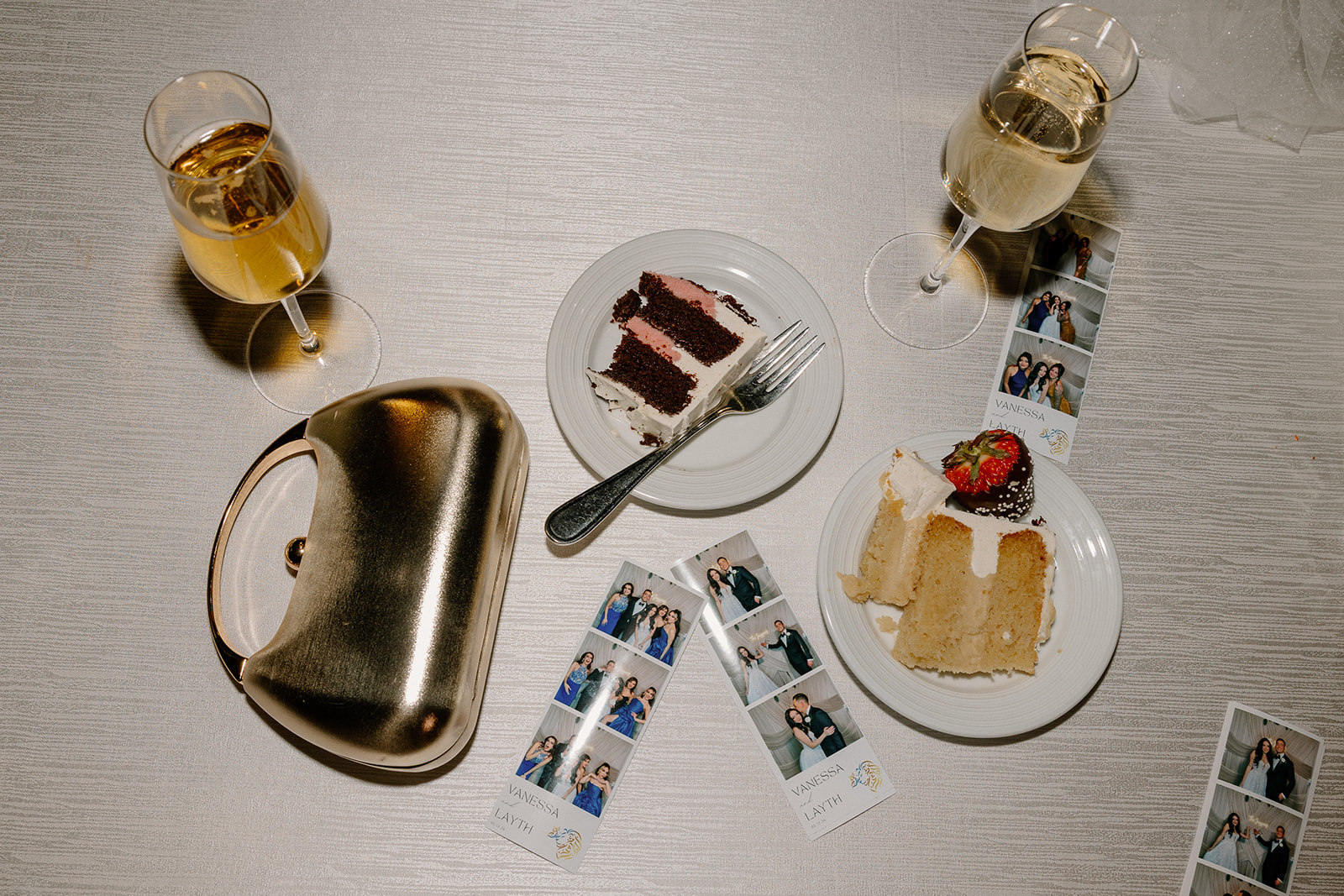 Wedding cake slices, champagne glasses, and photo booth strips laid out on a reception table
