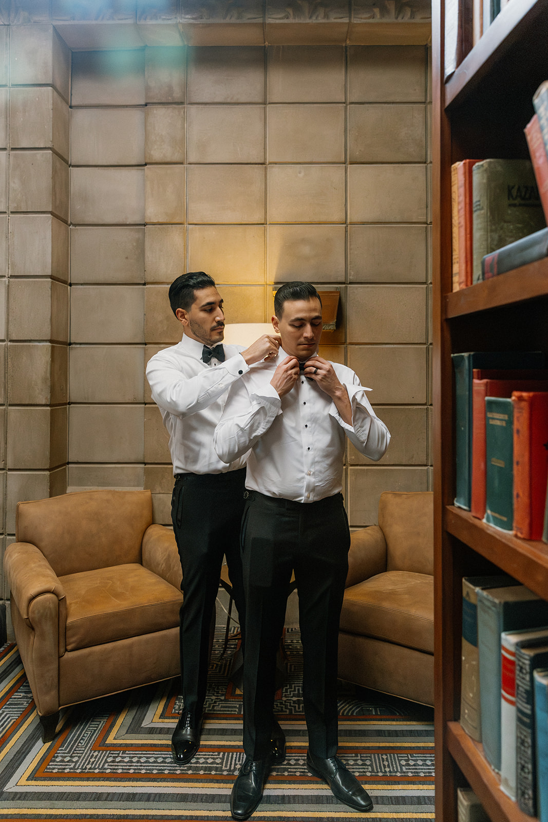 Groom getting help adjusting his bow tie from a groomsman in a lounge area
