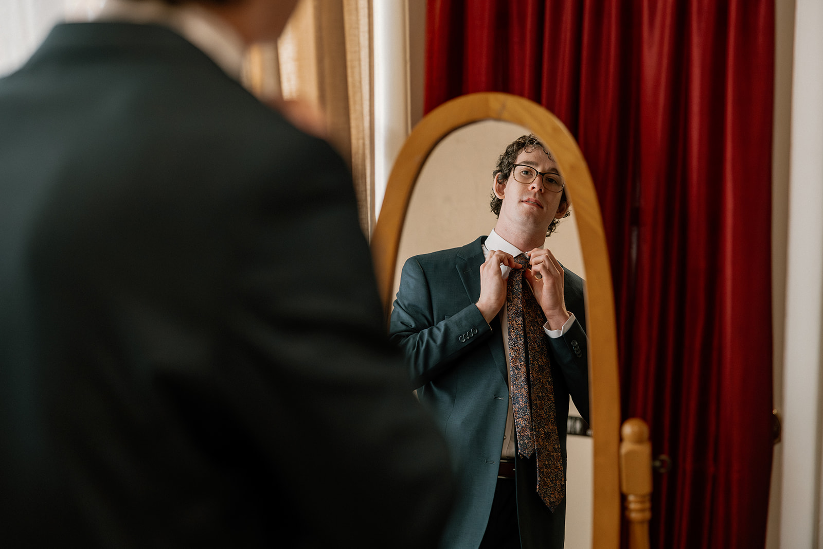 Groom looking at himself in the mirror while adjusting his tie before wedding ceremony at Boojum Tree Hidden Gardens Wedding Venue. 