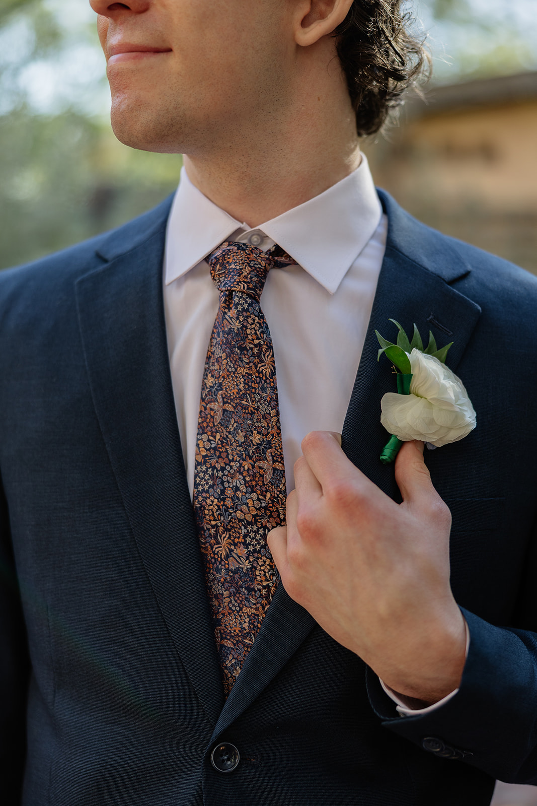 Groom adjusting tie and boutonniere in navy suit before ceremony at Arizona wedding venue
