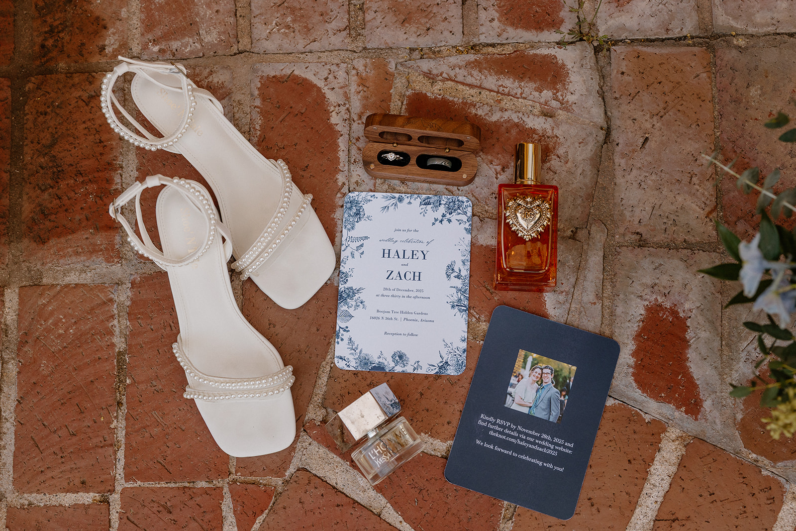 Wedding invitation suite with bride’s shoes, rings, and perfume styled on terracotta tile floor
