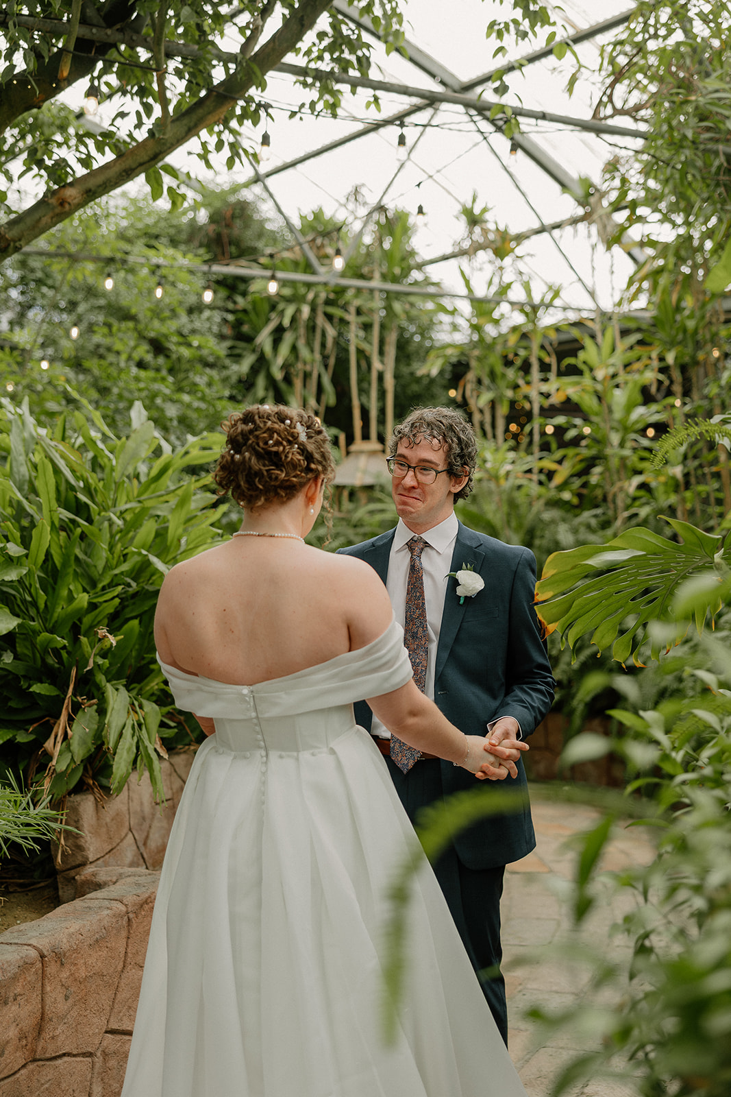 Couple holding hands and smiling at each other inside lush Arizona wedding venue greenhouse
