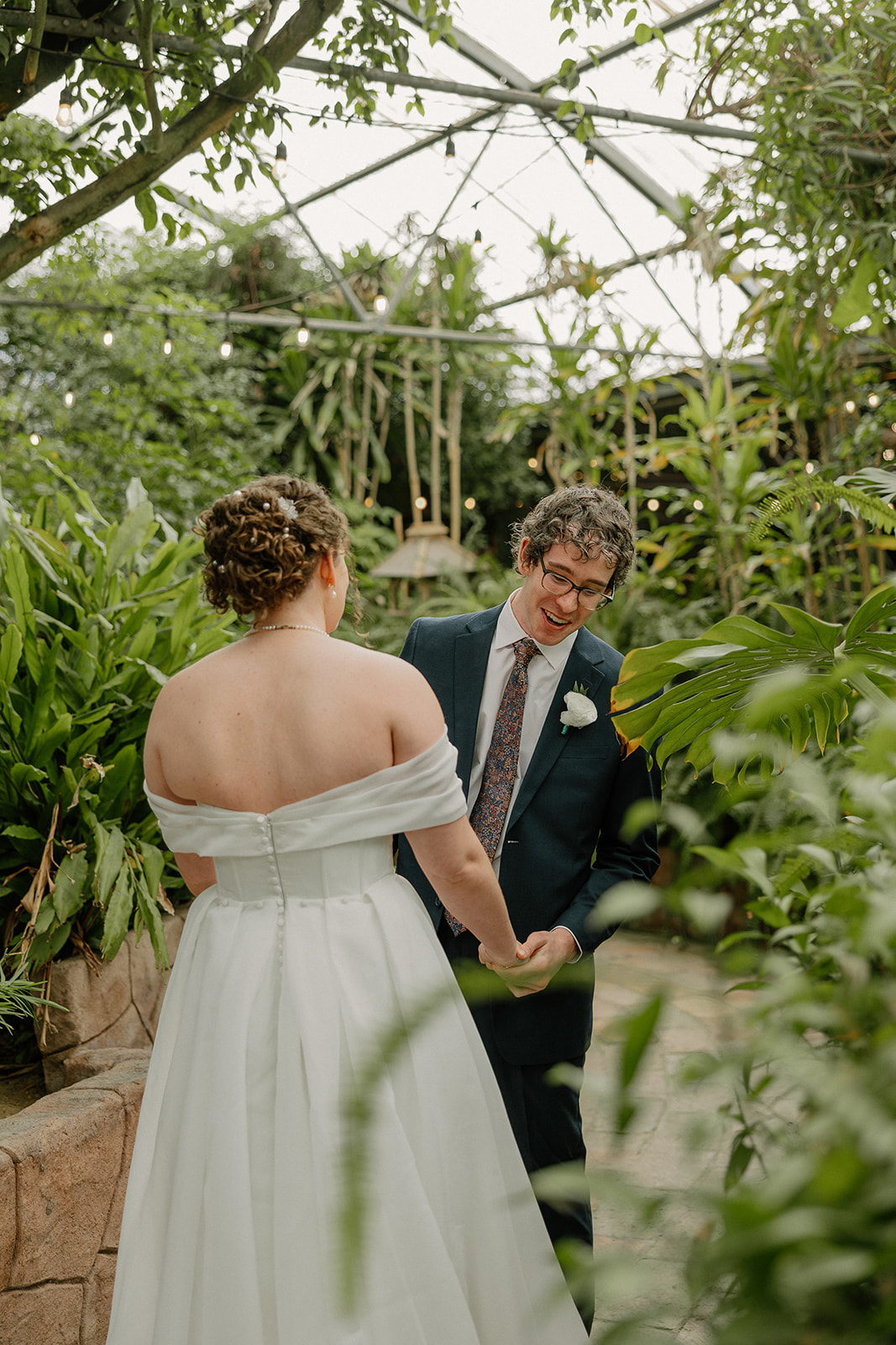Newlyweds laughing together while walking through greenery-filled Arizona wedding venues setting
