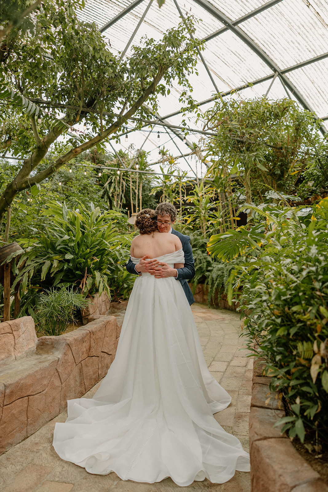 Bride and groom embracing in greenhouse filled with greenery and natural light after ceremony
