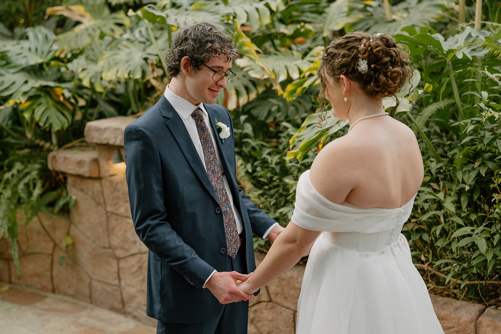 Couple holding hands and sharing a quiet moment in a greenery-filled Arizona wedding venue
