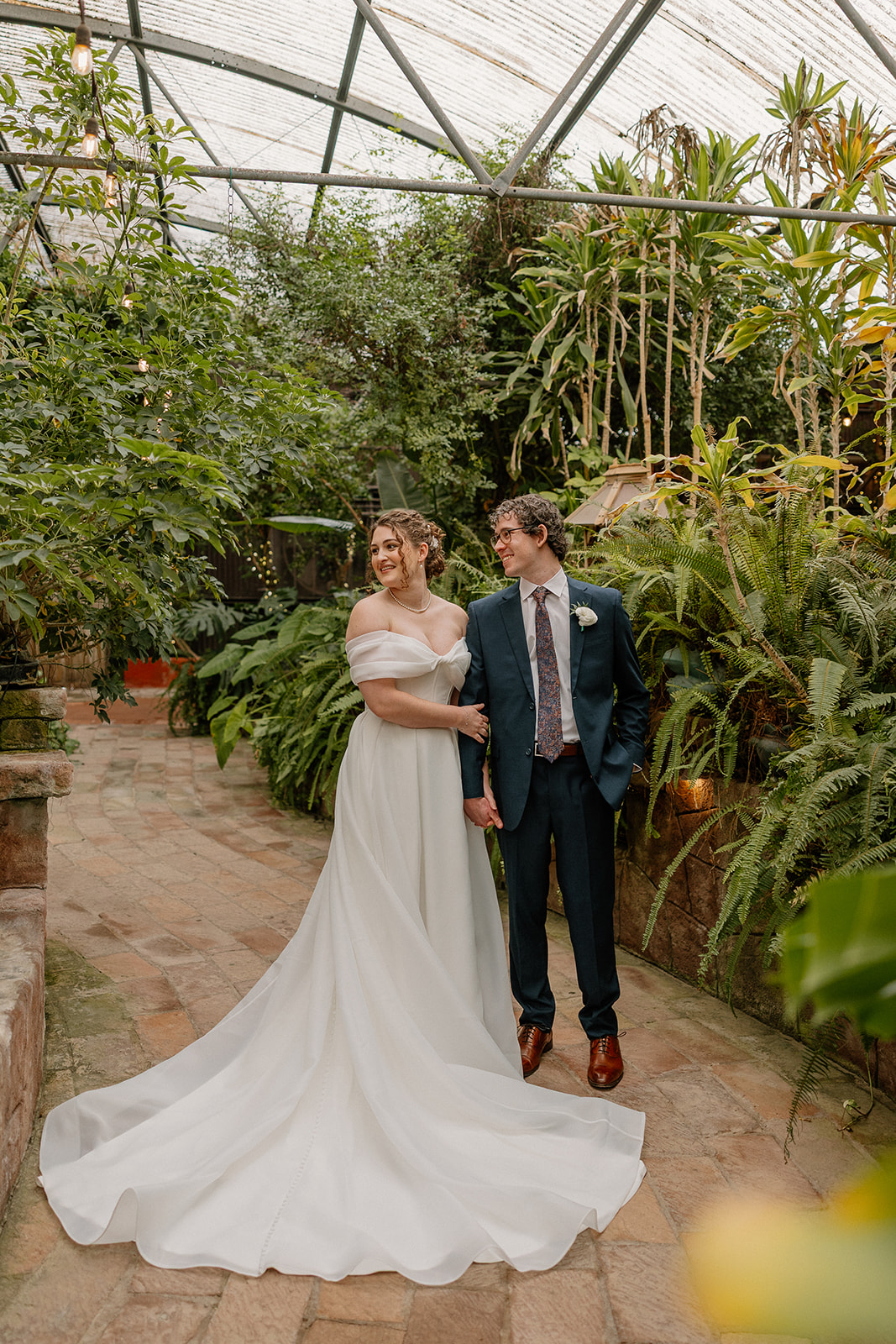 Bride and groom posing together in greenhouse at romantic Arizona wedding venue with lush greenery
