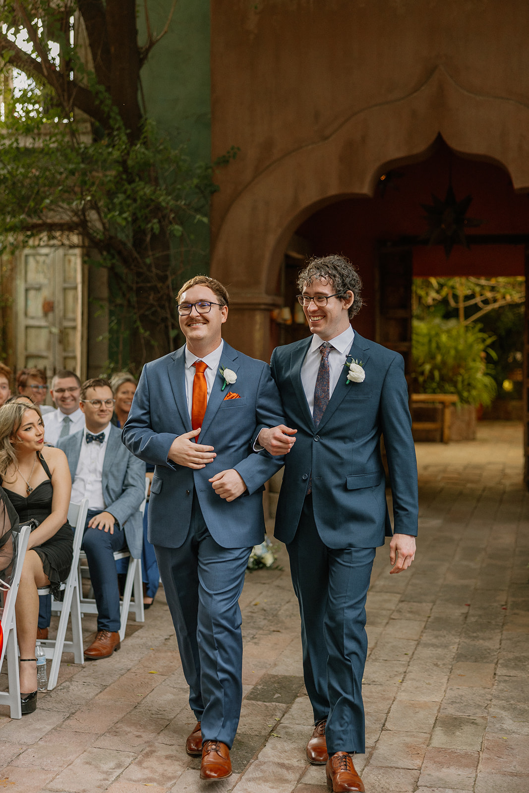 Groom walking down aisle with groomsman during ceremony at Arizona wedding venues with courtyard setting
