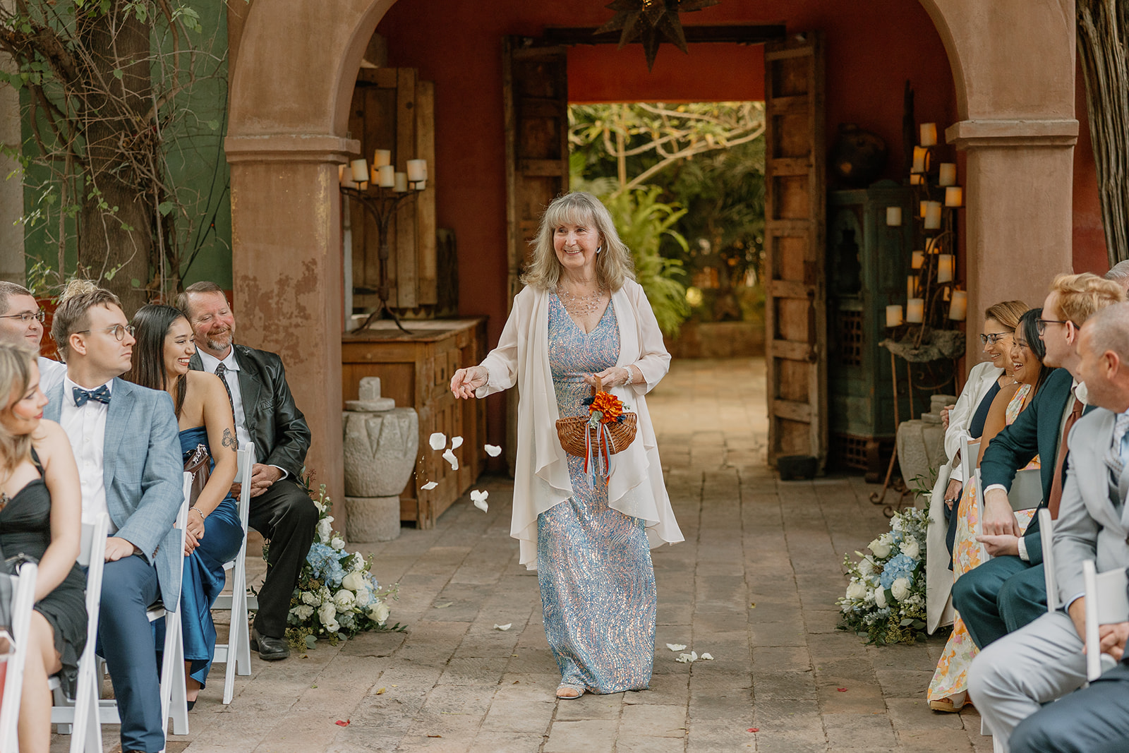 Flower girl tossing petals down aisle in charming Arizona wedding venue with rustic archway
