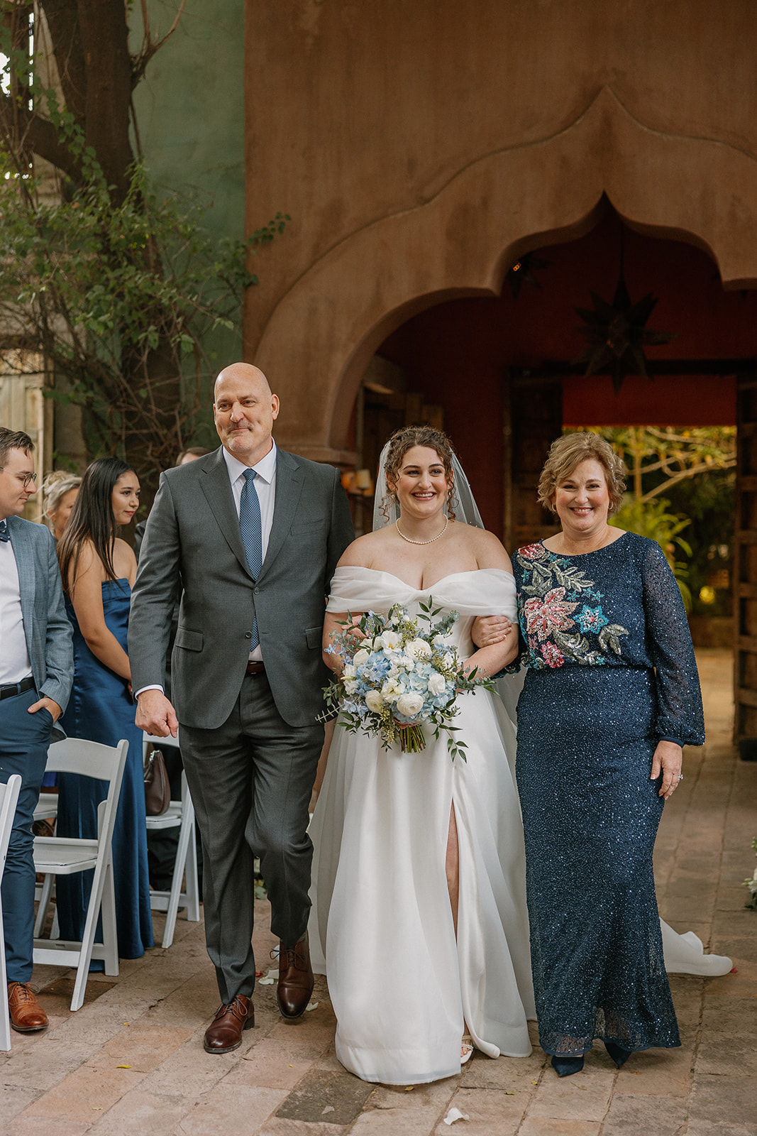 Bride walking down the aisle with parents at romantic Arizona wedding venue with warm adobe architecture
