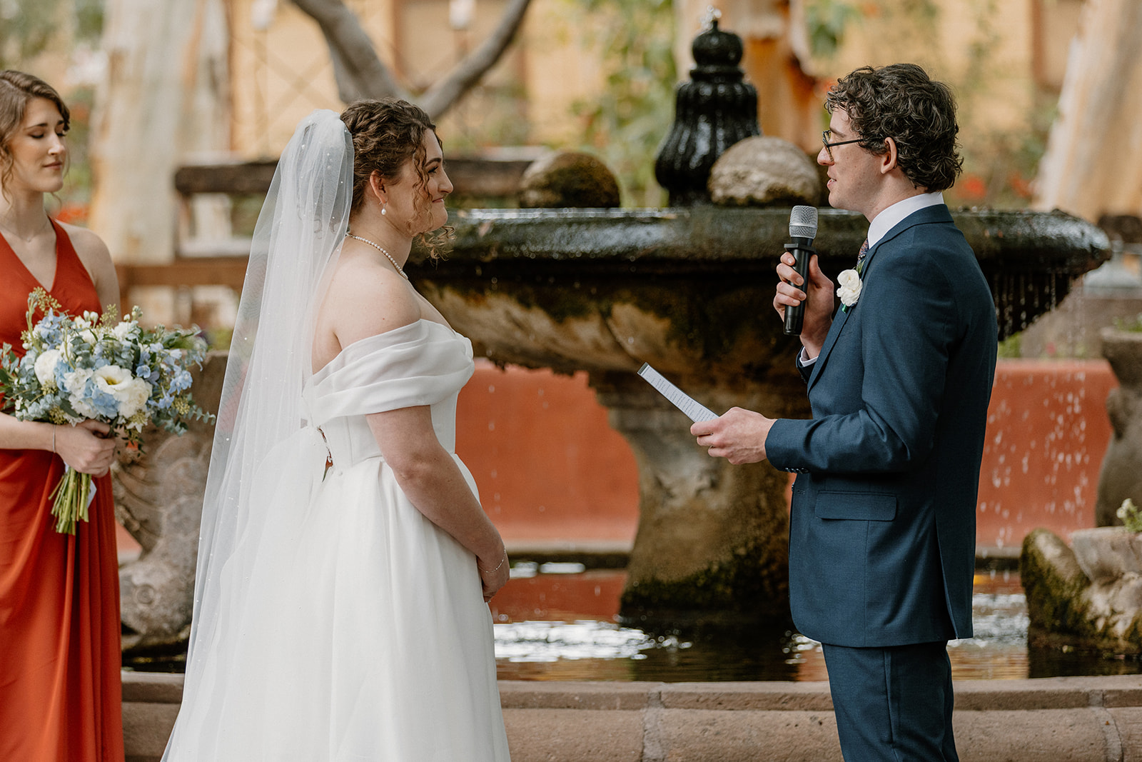 Groom reading vows to bride during intimate ceremony at Arizona wedding venue with stone fountain
