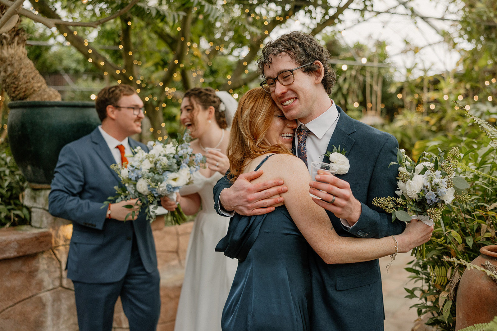 Groom hugging guest during cocktail hour with string lights and greenery at Arizona wedding venues
