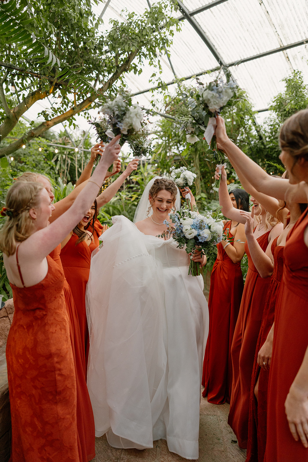 Bride walking under raised bouquets from bridesmaids in a joyful Arizona wedding venue celebration
