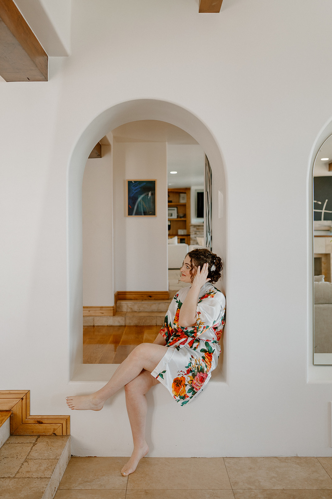 Bride in floral robe sitting in arched doorway during relaxed getting ready photos
