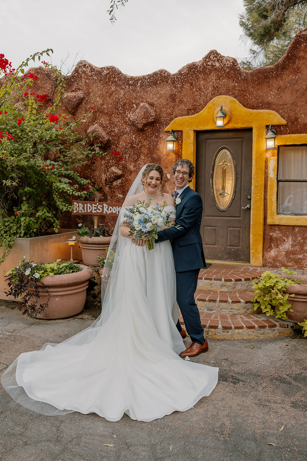 Bride and groom smiling outside adobe-style building at Arizona garden wedding venue
