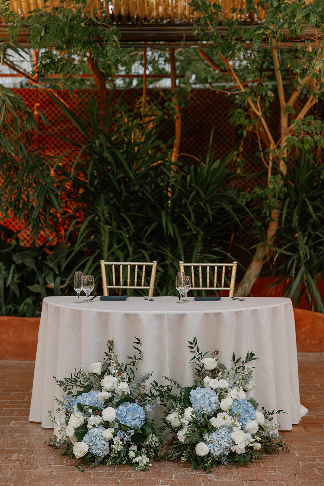 Sweetheart table with blue and white florals at Arizona wedding venue with tropical garden backdrop
