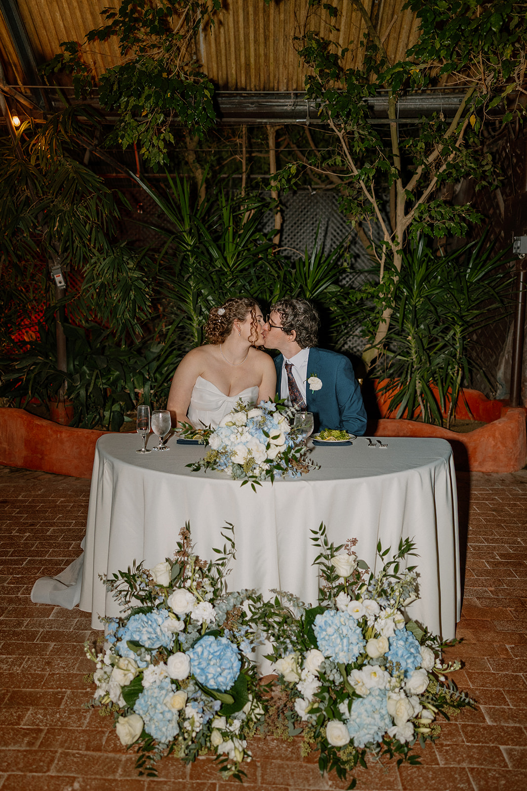 Bride and groom kissing at sweetheart table with floral arrangements at Arizona wedding venues reception
