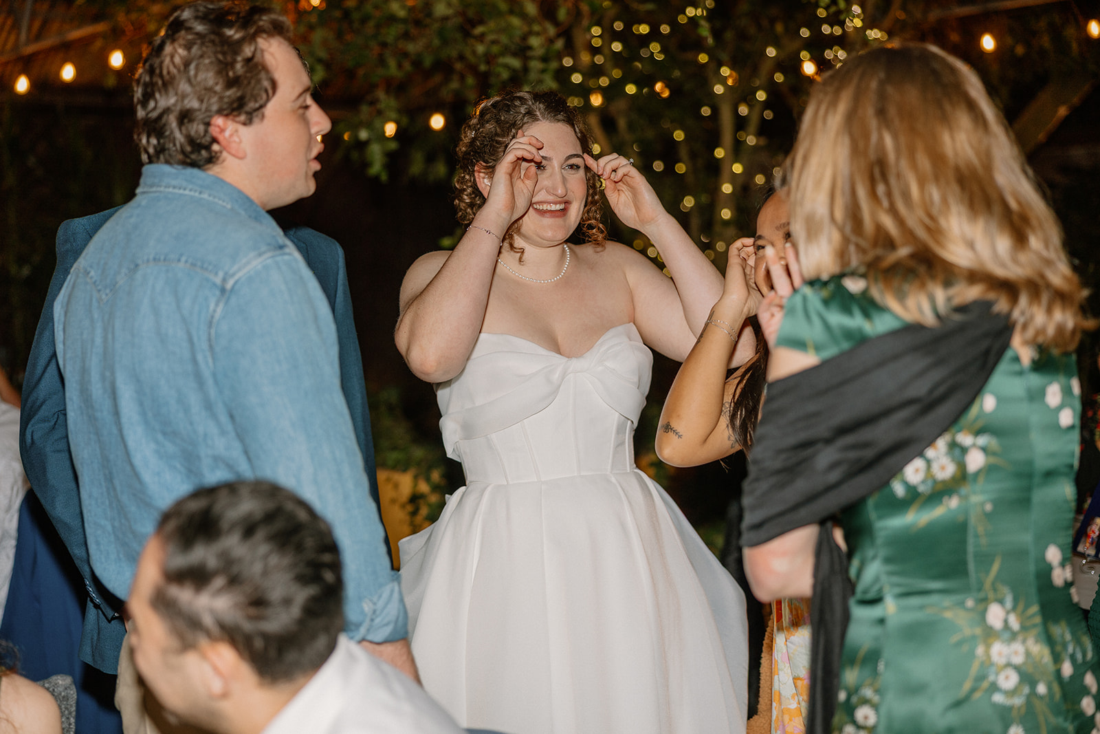 Bride laughing with guests on the dance floor surrounded by warm string lights and evening ambiance
