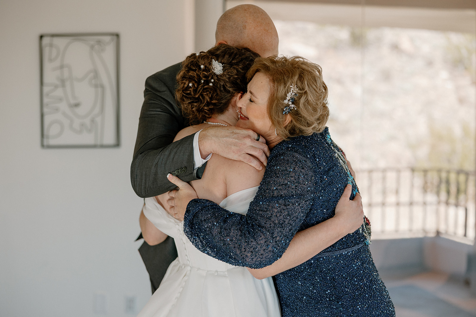 Bride embracing parents in heartfelt moment before ceremony in natural light-filled room

