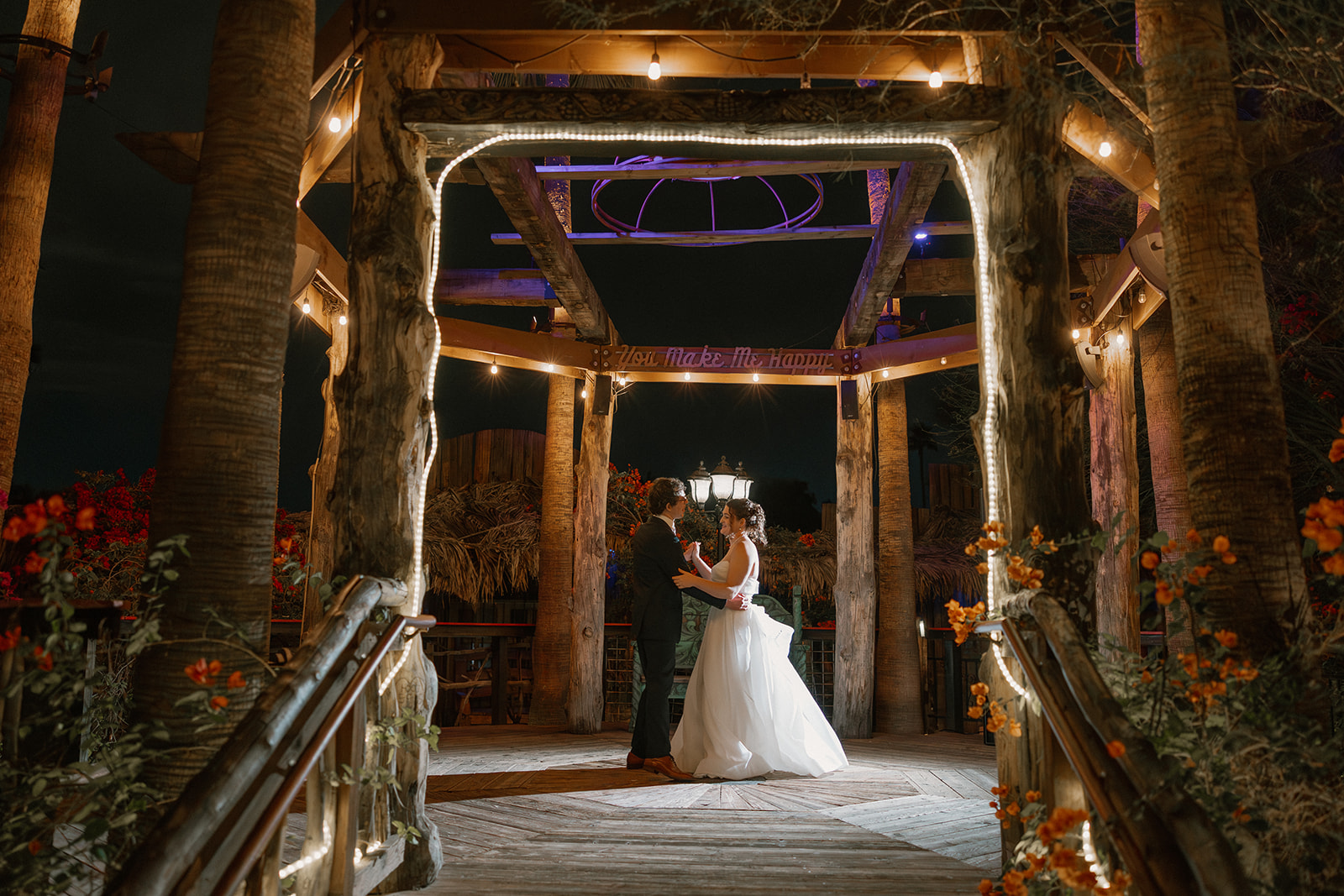 Bride and groom dancing under a wooden pergola with string lights at a romantic Arizona wedding venue at night
