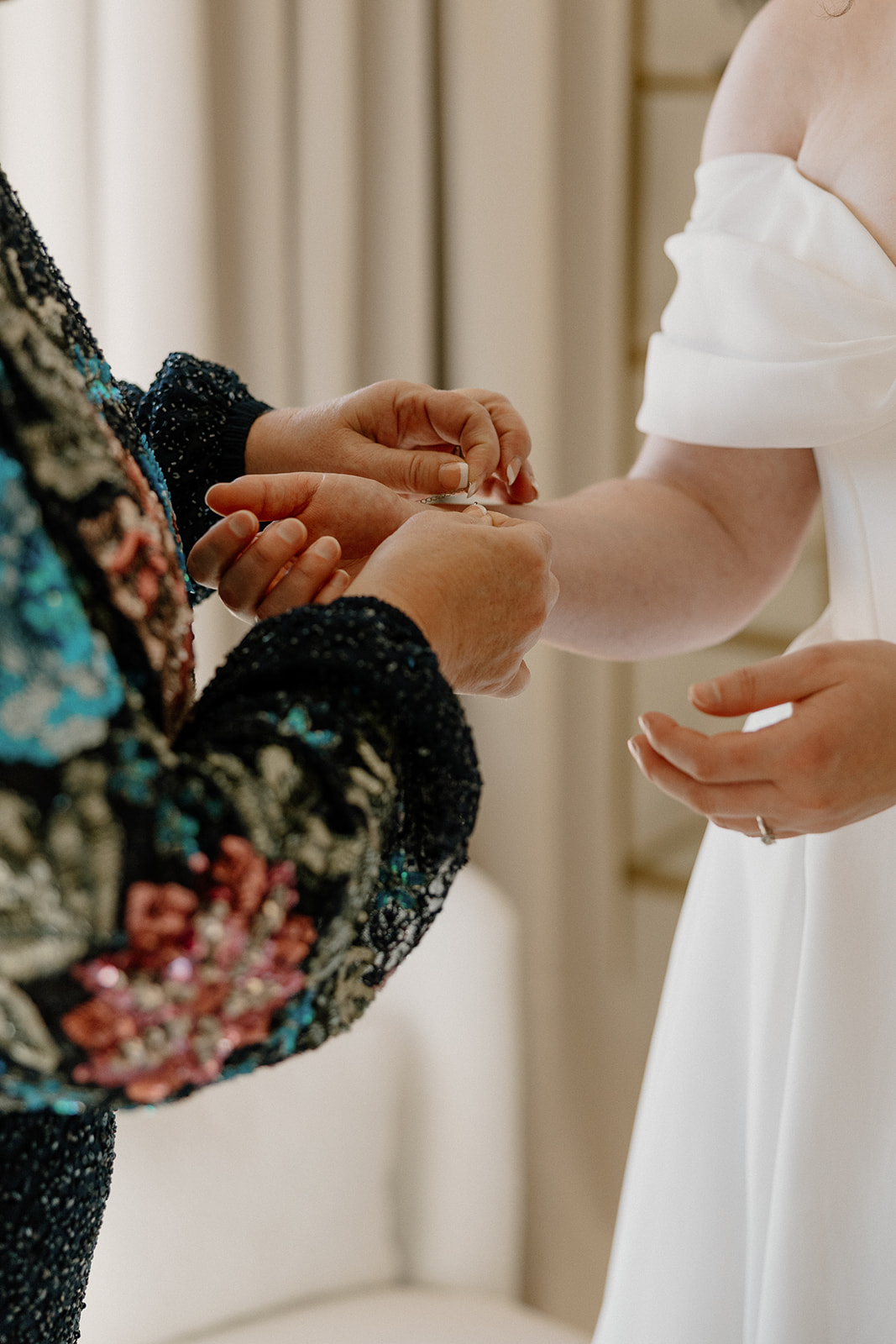 Close-up of mother fastening bracelet on bride’s wrist during emotional wedding morning prep
