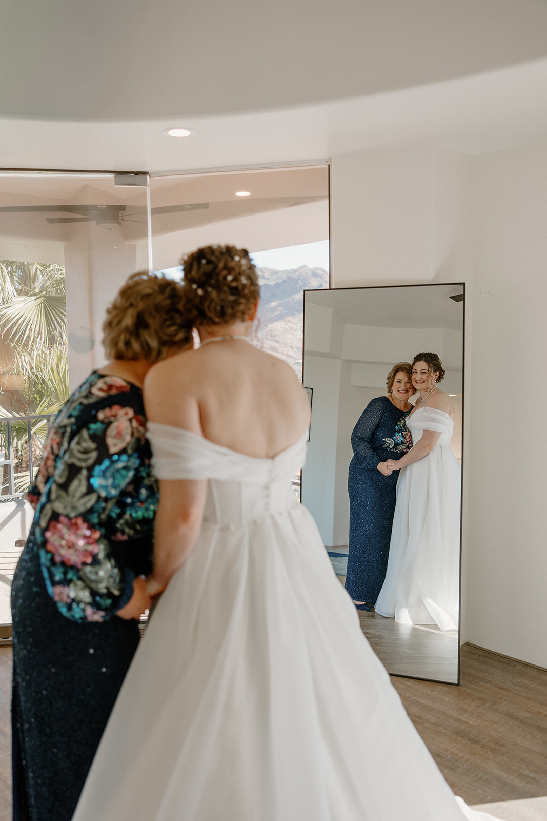 Bride and mother smiling together in mirror during getting ready moments before Arizona wedding
