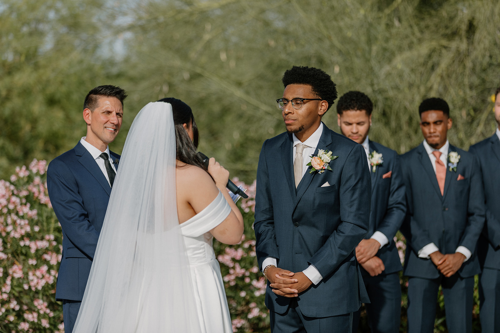 bride speaking vows to groom during outdoor ceremony with wedding party in background
