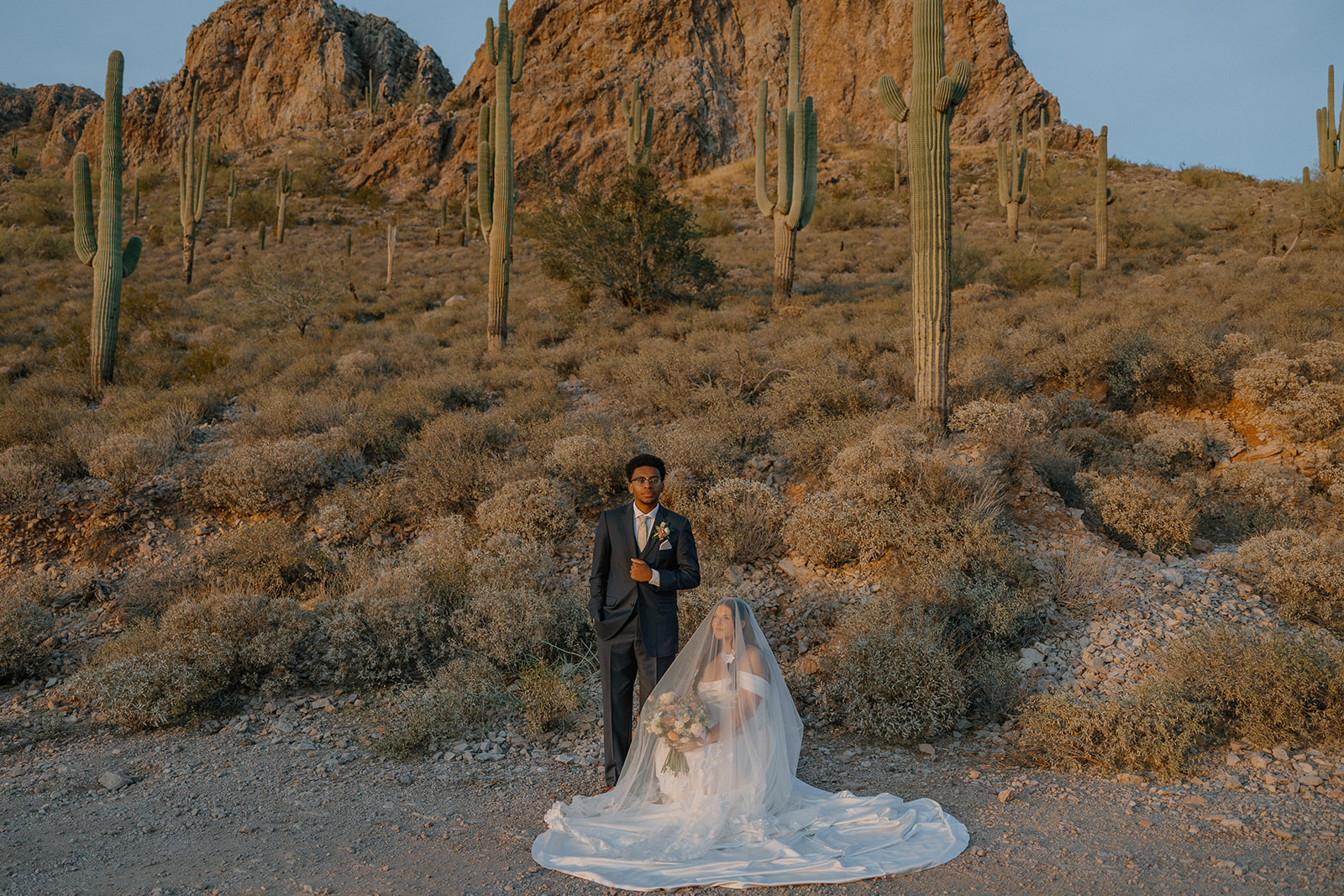 bride and groom posing in desert landscape with cactus and mountains during golden hour at gold canyon golf resort wedding
