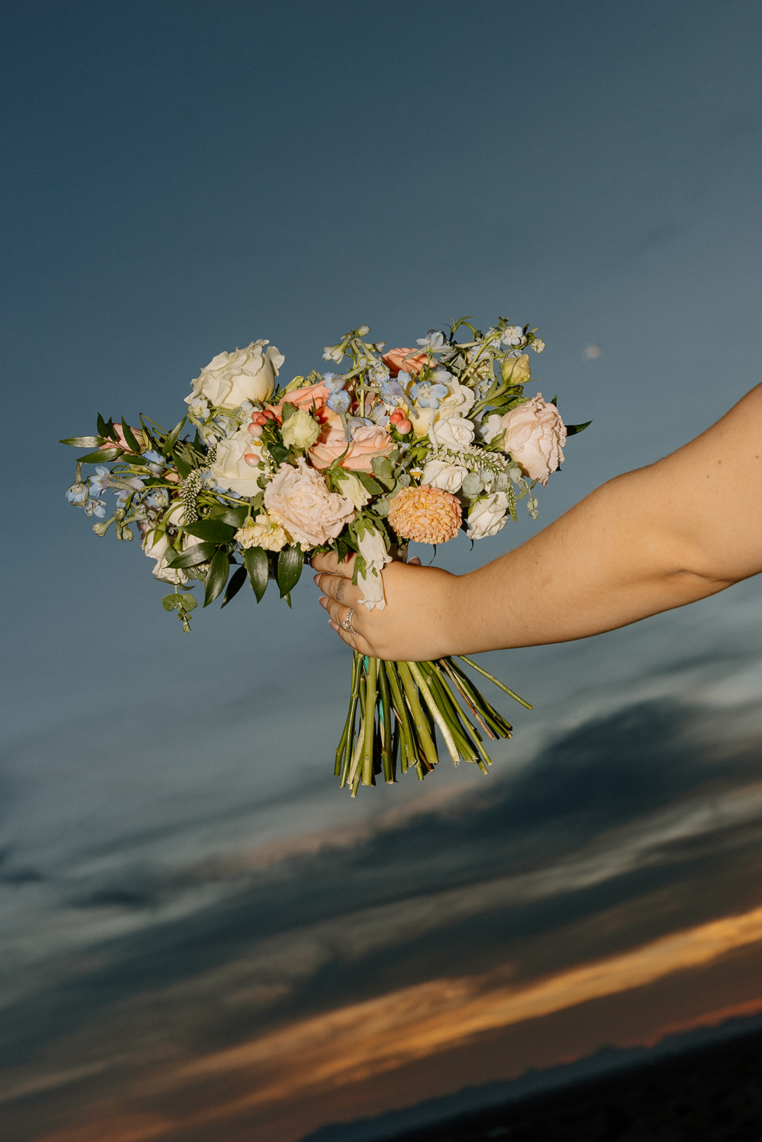 close up of wedding bouquet with pastel flowers against sunset sky