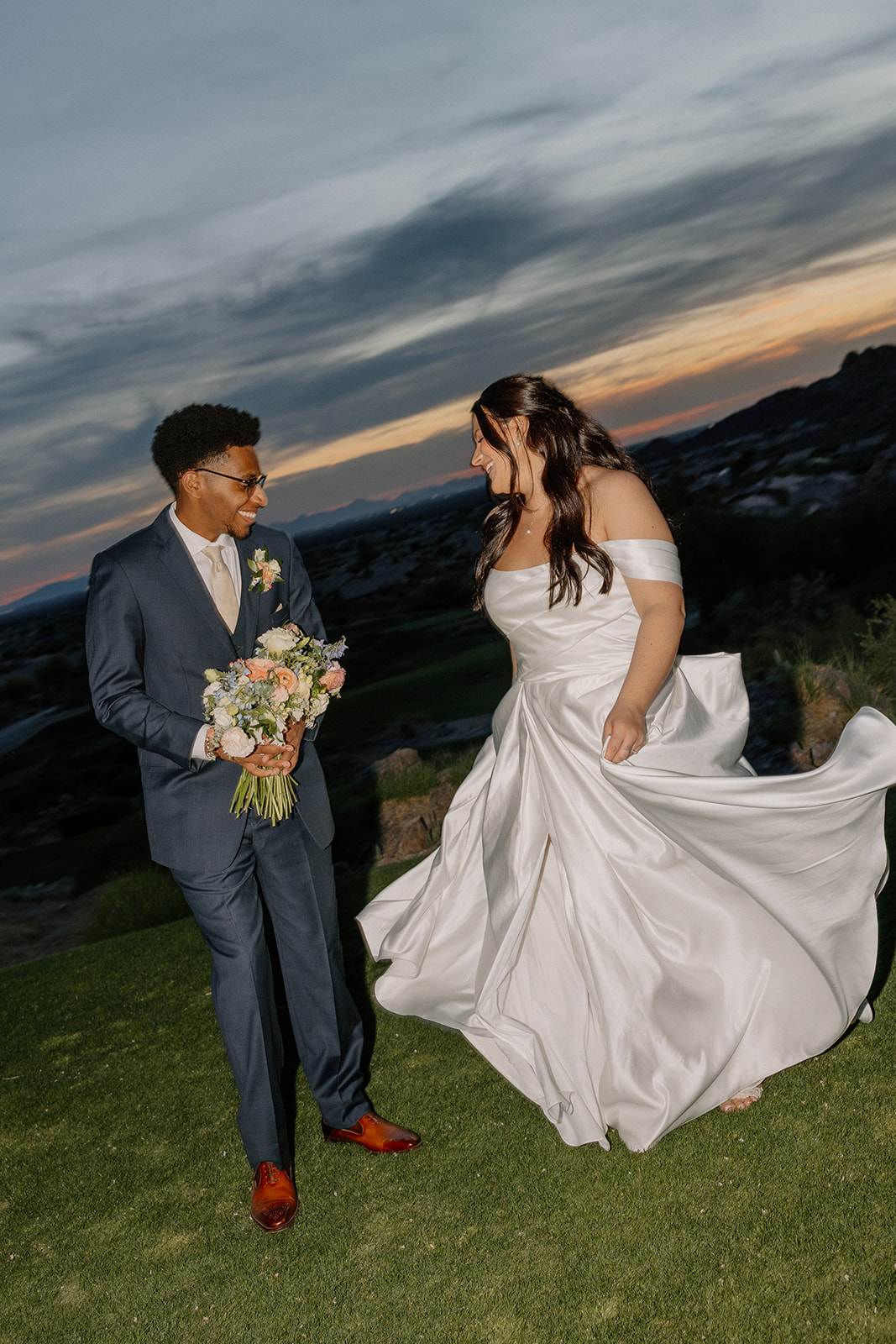 bride and groom walking together at sunset with mountains and dramatic sky in background at gold canyon golf resort wedding
