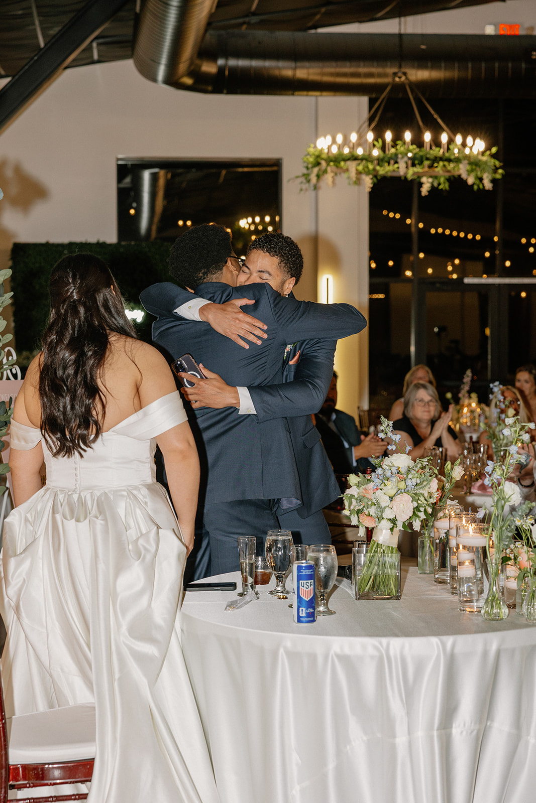 groom hugging family member during reception with guests watching in background