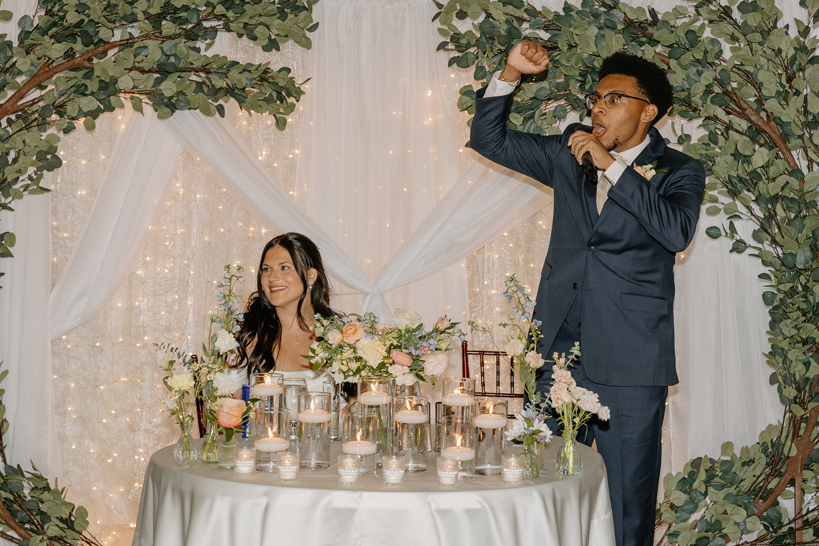couple sitting at sweetheart table during reception with candles and floral decor
