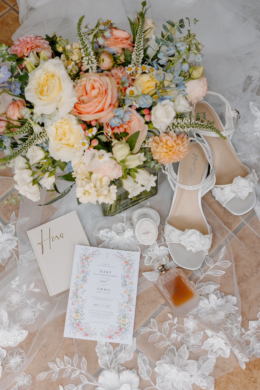 flat lay of wedding details including invitation, shoes, perfume, and floral arrangement