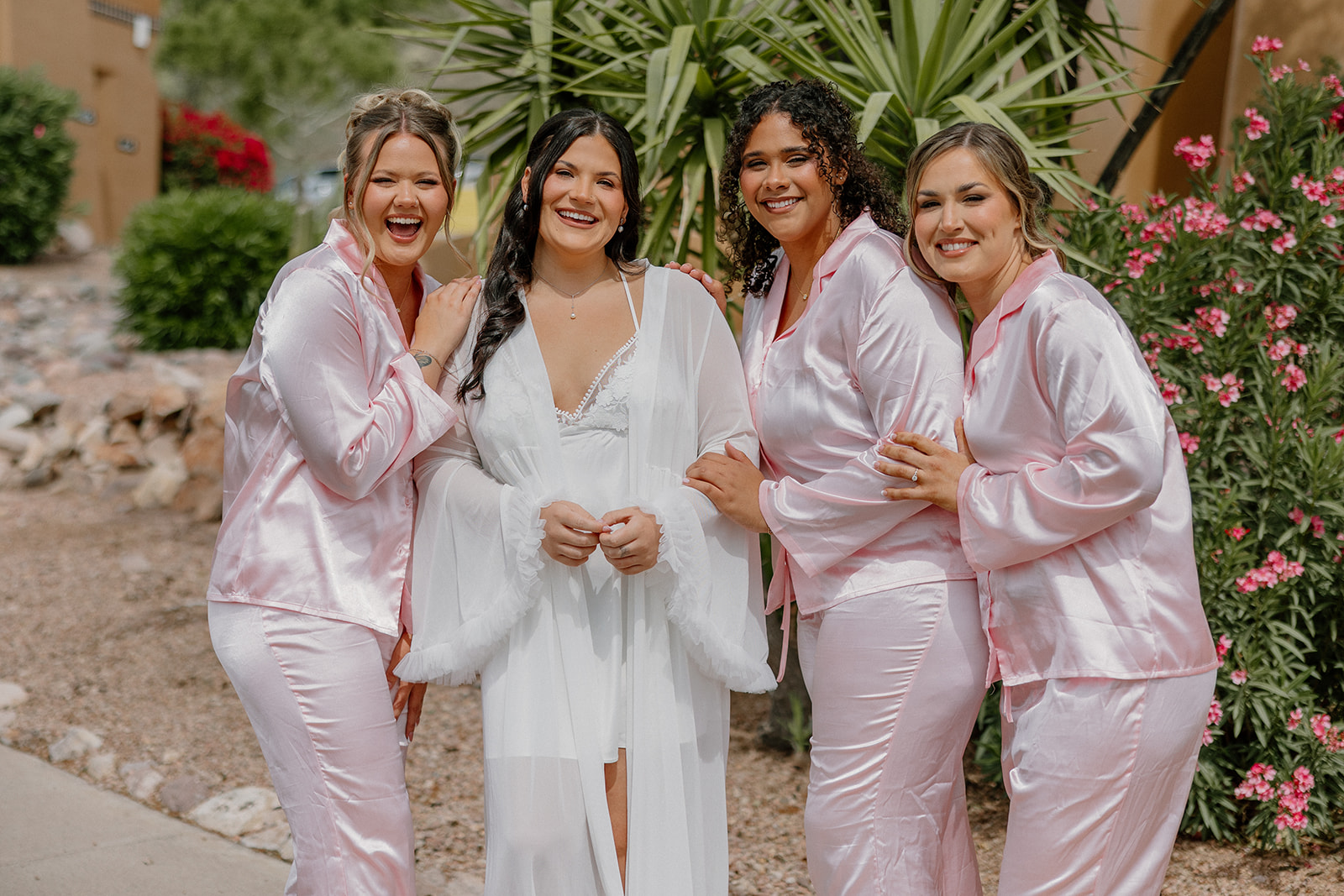 bride and bridesmaids in matching pink pajamas smiling together outdoors
