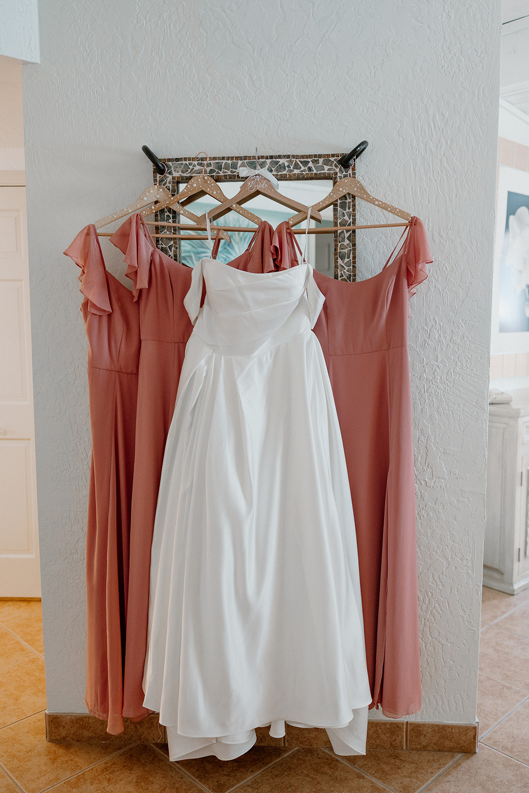 wedding dress and bridesmaid dresses hanging together in getting ready space