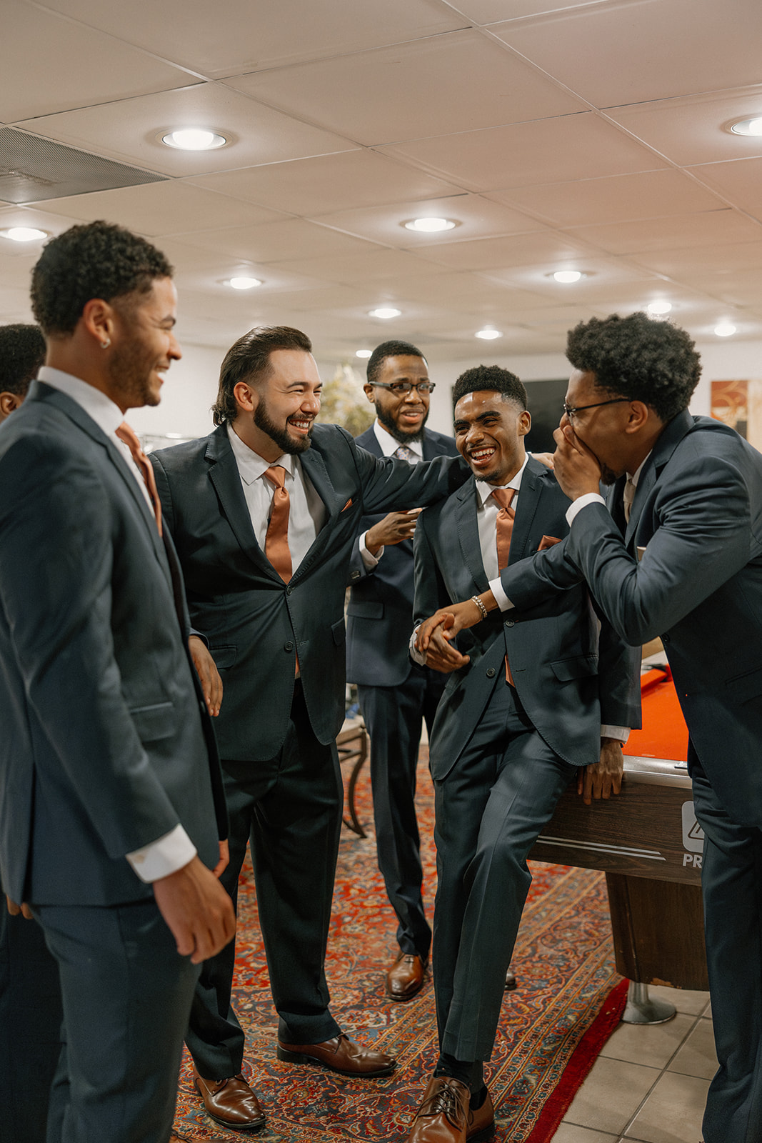 groomsmen laughing together while getting ready in suit jackets and ties