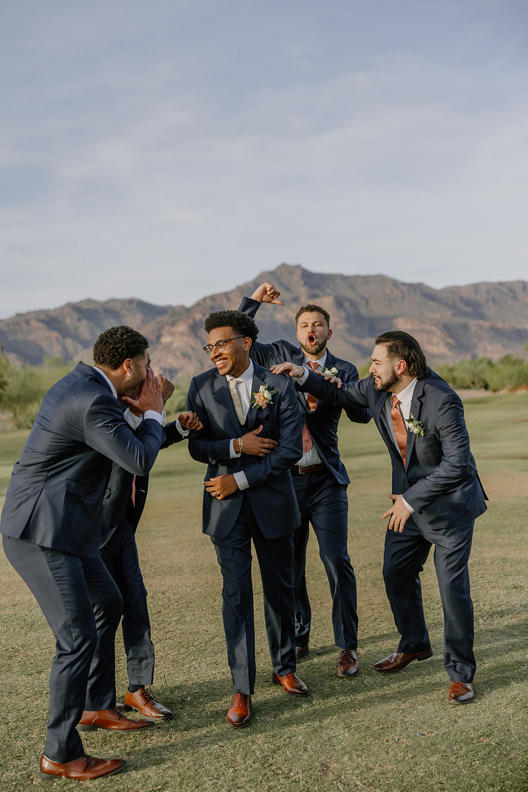 groom and groomsmen laughing together outdoors with mountain views