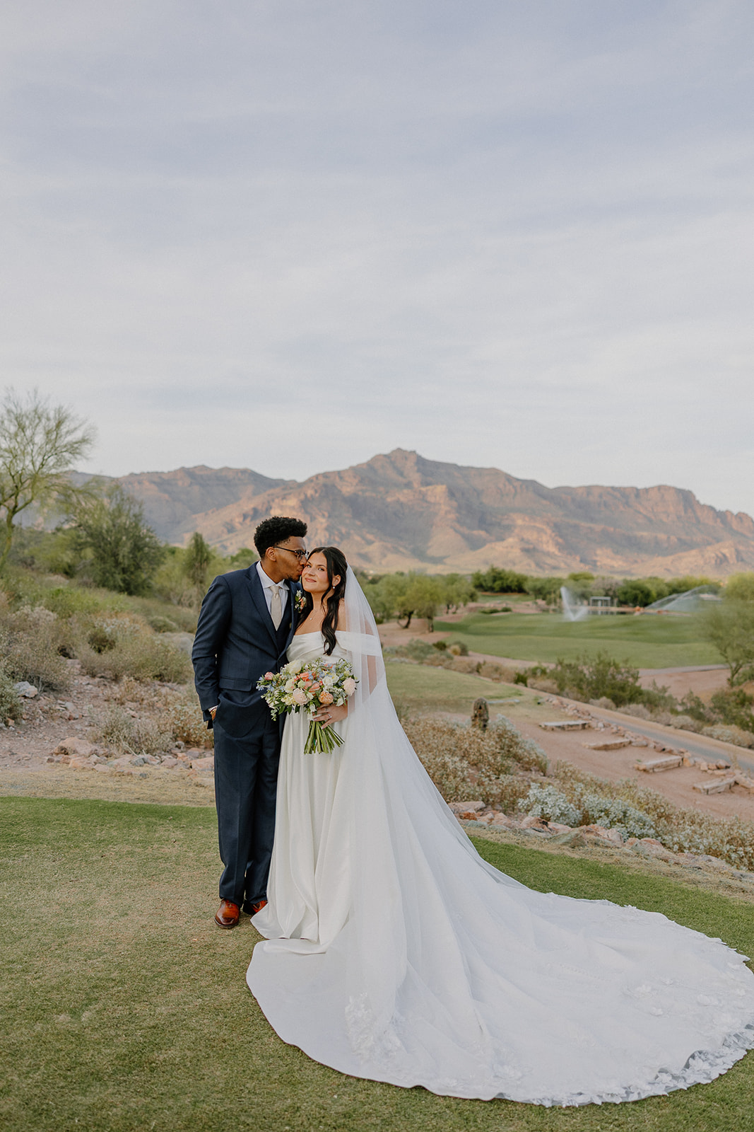 bride and groom posing together with long veil and mountain views at gold canyon golf resort wedding