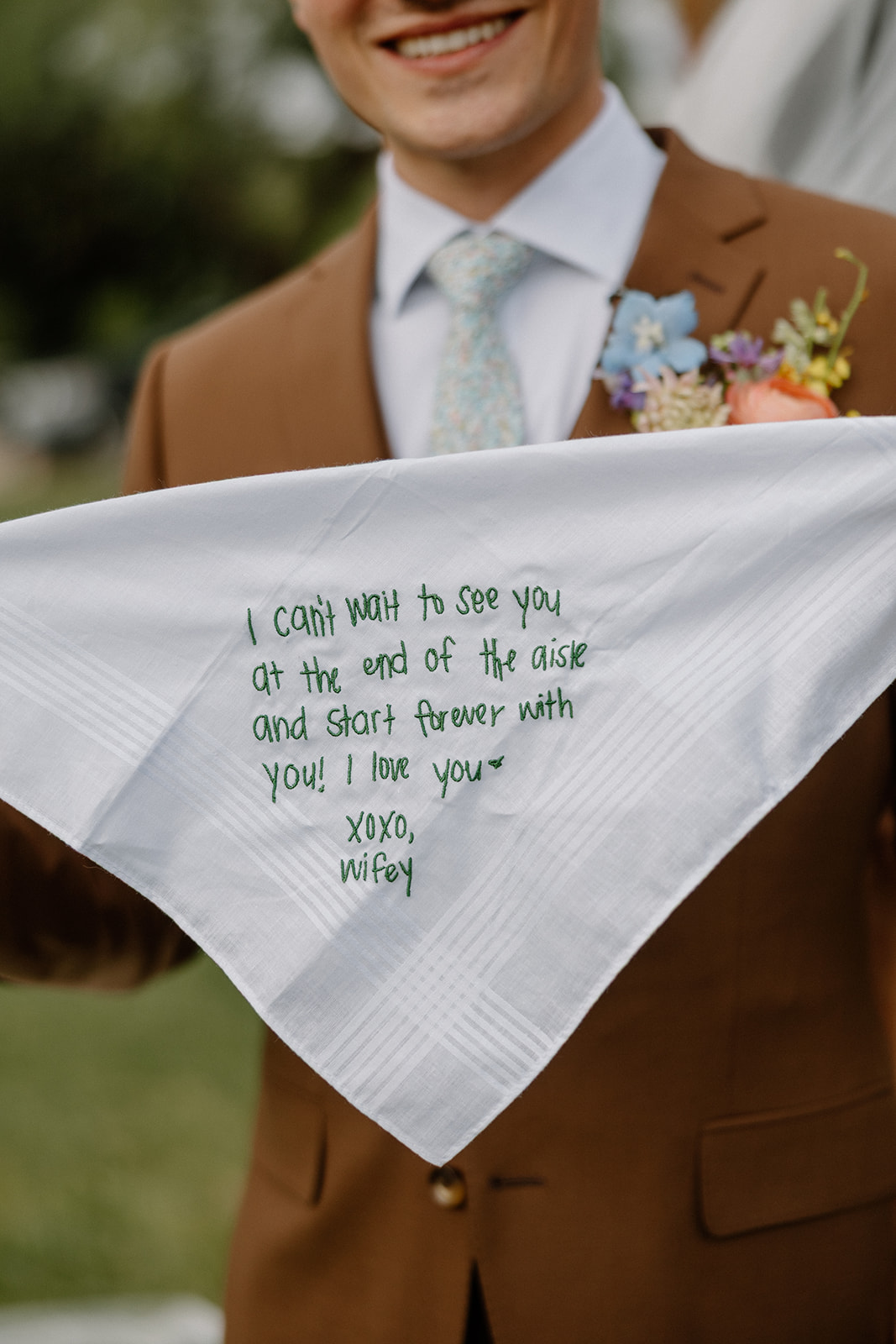 A groom holding up a wedding detail, an embroidered handkerchief from his wife