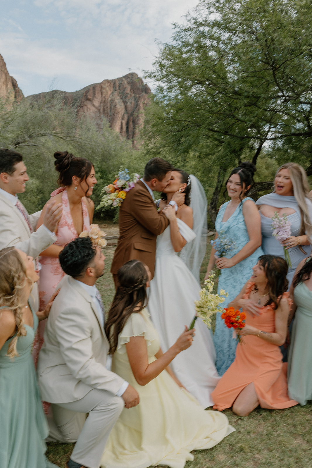 A bride and groom kissing in the middle of their wedding party