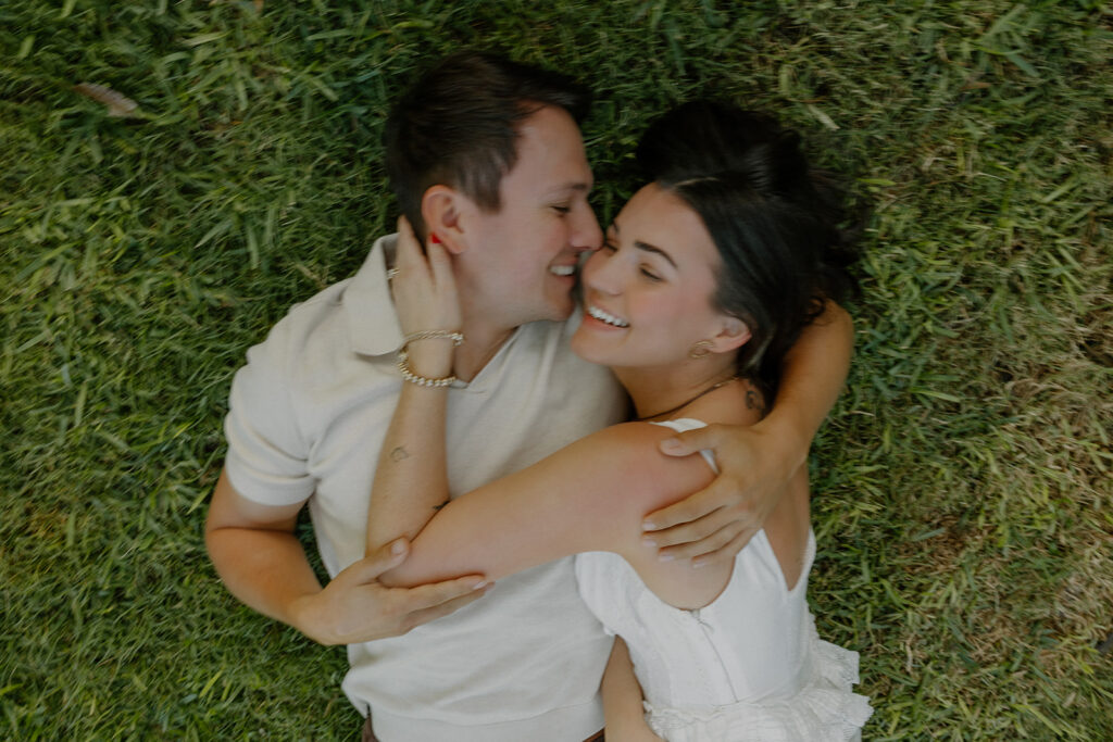 A couple laughing during blurry romantic engagement photo in the grass