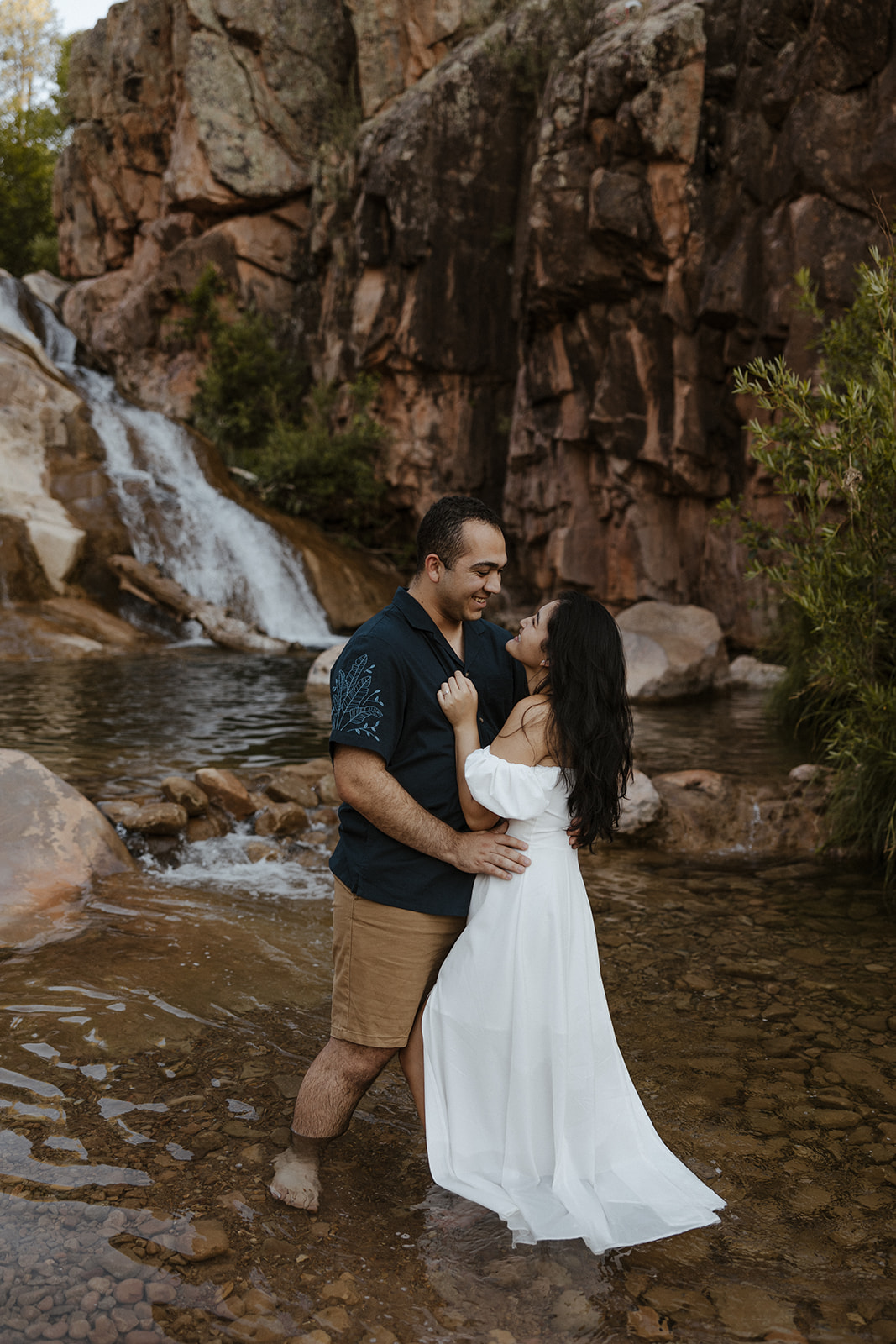 A couple taking summer engagement photos at an engagement photo location with a waterfall