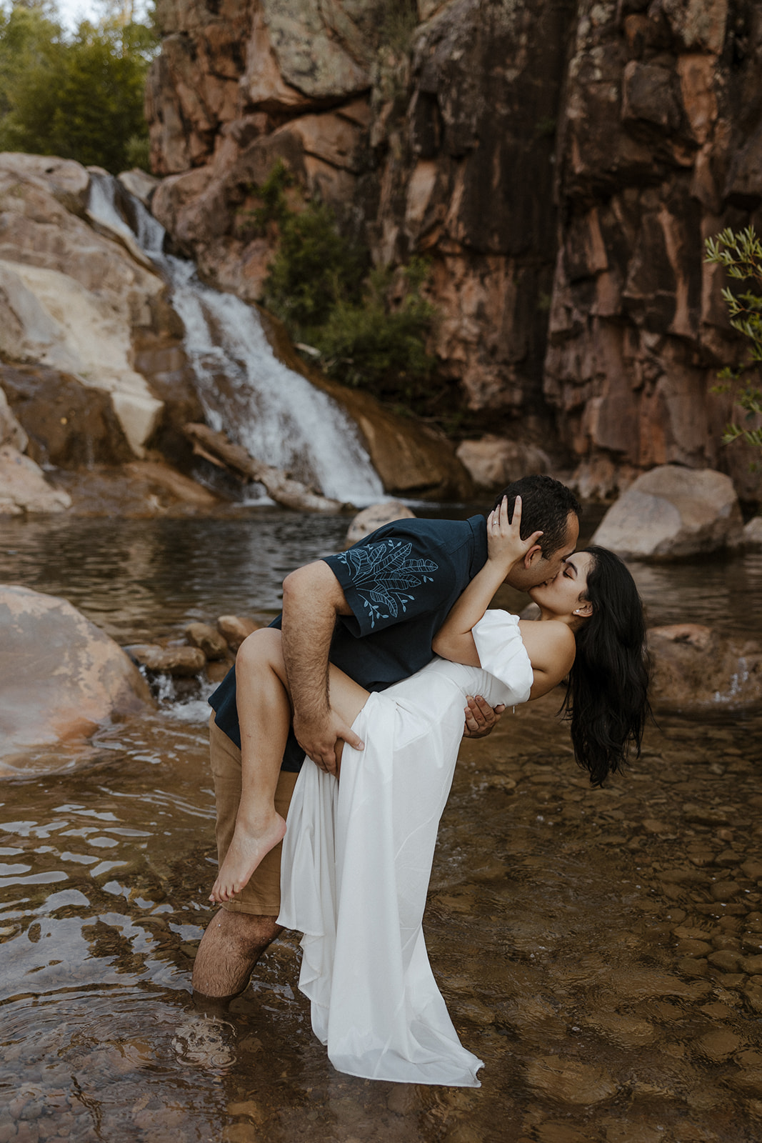 A couple taking summer engagement photos at an engagement photo location with a waterfall